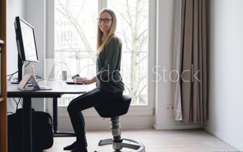 Frau sitzt auf beweglichem Schreibtischstuhl im Homeoffice
