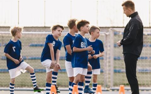 Fußballtrainer trainiert mit einer Gruppe Jungen in Fußballtrikots auf dem Fußballplatz