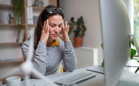 Frau mit Kopfschmerzen sitzt vor dem PC und reibt sich die Schläfen
