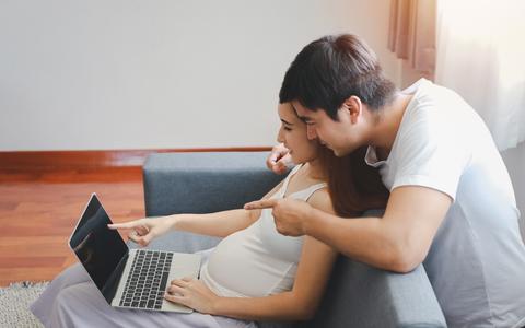 Schwanger Frau und Mann betrachten zusammen Laptop