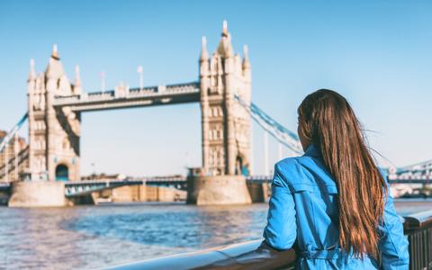 Junge Frau steht mit Rücken zur Kamera bei Sonnenschein vor der Towerbridge in London